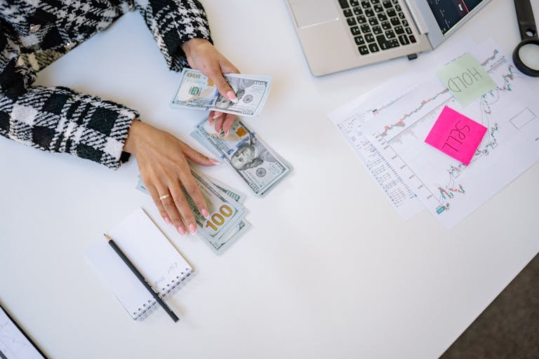 Businesswoman counting dollar bills with financial charts and laptop on table. Investment and finance concept.