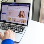 Hands typing on a laptop with an e-commerce website open, showcasing online shopping.